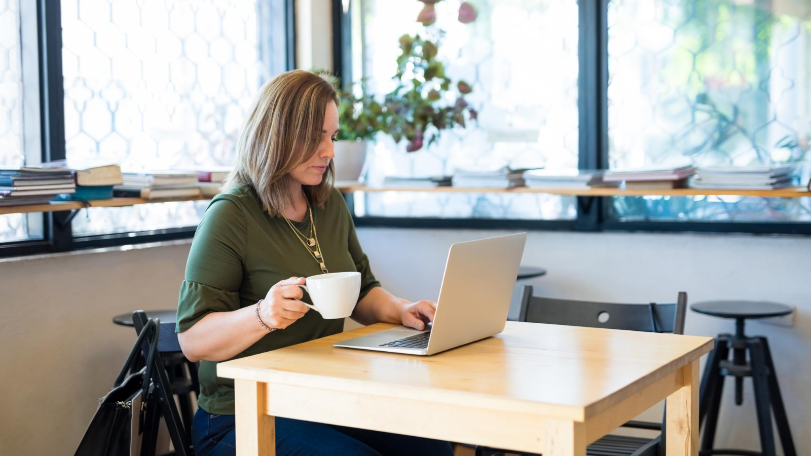 woman sitting at a desk with a cup of coffee, researching and writing on her laptop for a blog