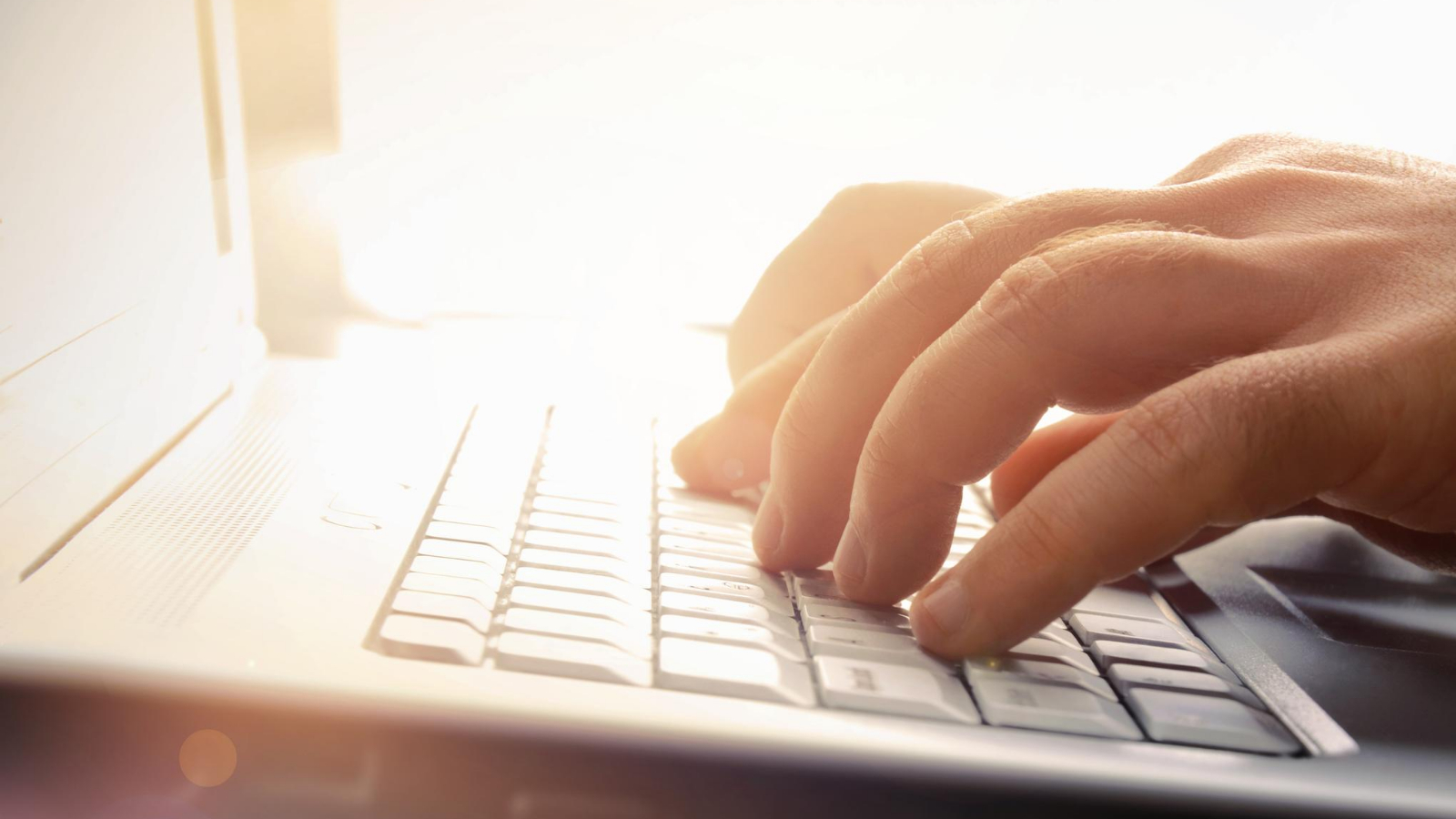 a person's hand rests on a laptop keyboard as he types